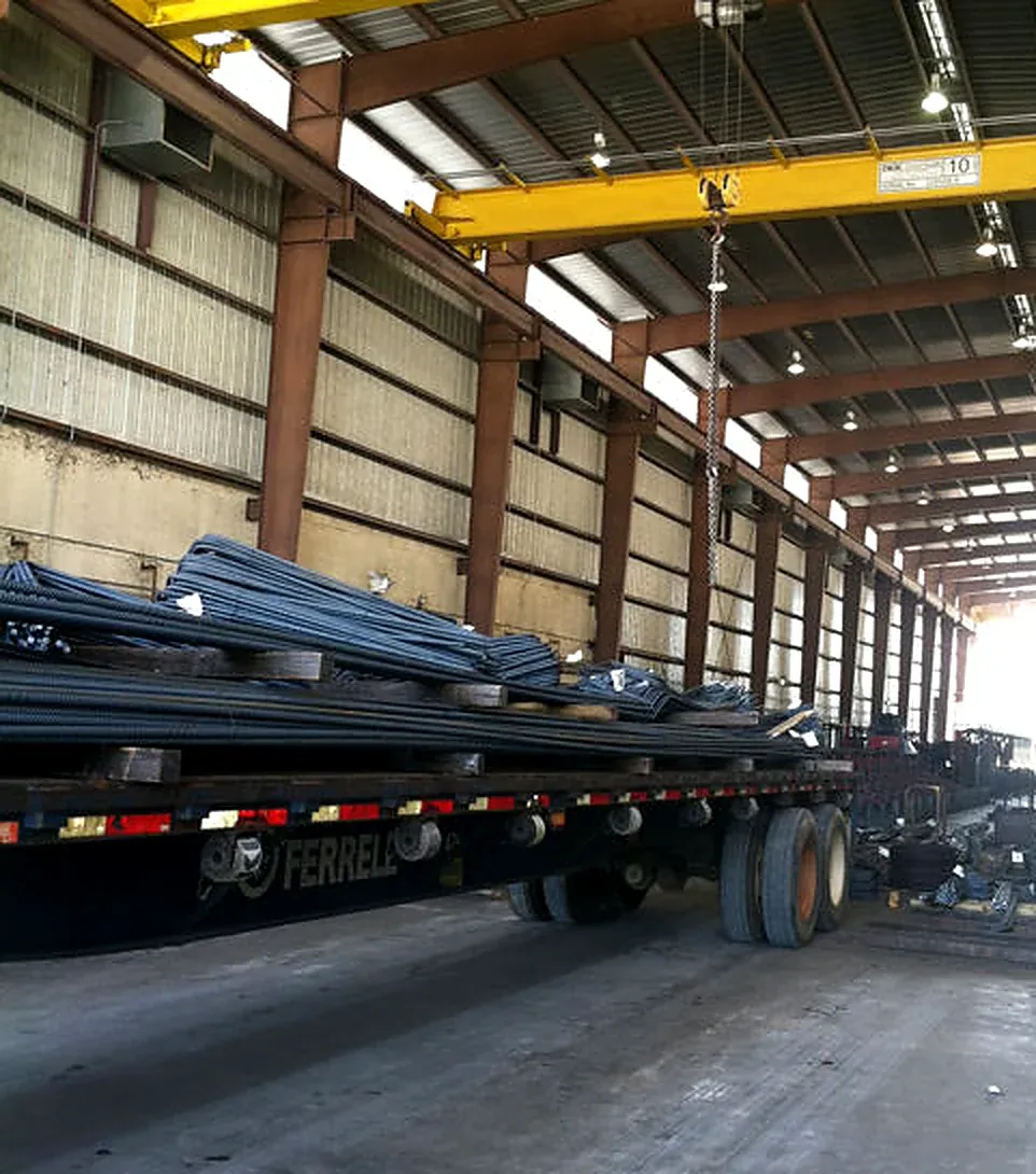 Shop interior with an overhead crane and a flatbed trailer loaded with bundled reinforcing steel