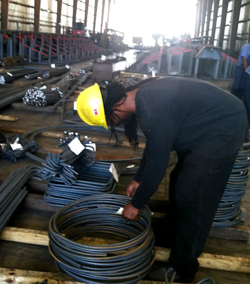 Worker in a yellow hard hat handling coiled reinforcing steel