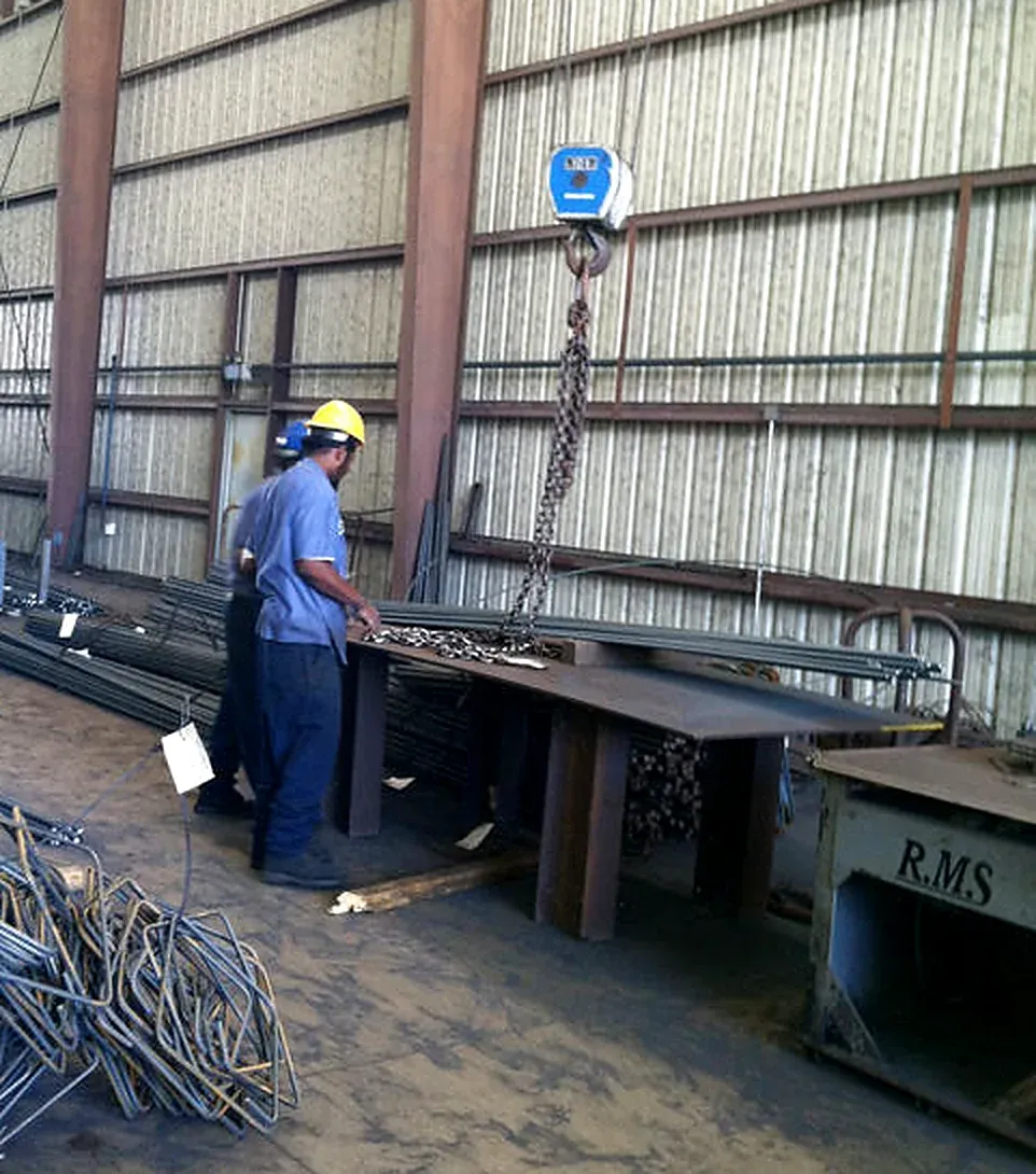 Worker beside a hanging crane scale, with bent reinforcing steel in the foreground